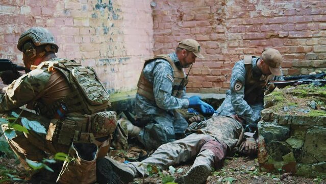 Soldiers man with machine gun stand on position. On background combat medic provides first aid to wounded soldier. Military concept