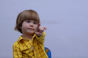 Positive little boy in a yellow shirt points his finger. Pointing finger. Space for text