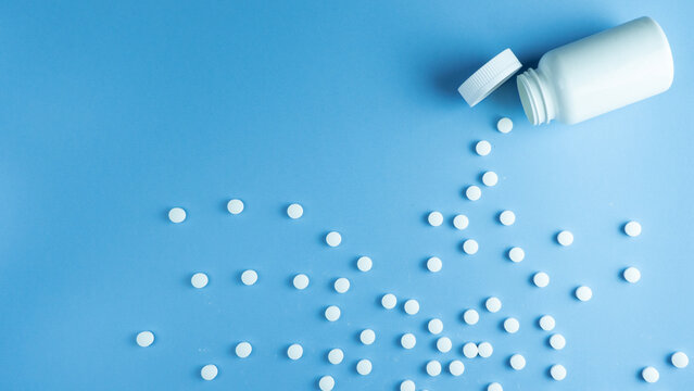 Vitamin pills flatlay on a blue background in a plastic white bottle. Vitamin medical prescription.