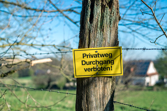An einem Stacheldrahtzaun hängt ein gelbes Schild mit der Aufschrift "Privatweg Durchgang verboten!"