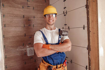 Cheerful male builder standing by the wall with ceramic tile