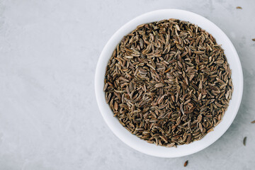 Cumin seeds or caraway in white bowl on gray stone background