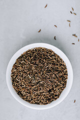 Cumin seeds or caraway in white bowl on gray stone background