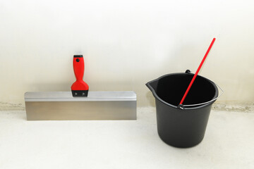 Clean spatula (trowel ), whisk for plaster in an empty bucket against the backdrop of a concrete wall. Construction finishing works