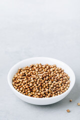Coriander whole dry seeds in white bowl on gray stone background