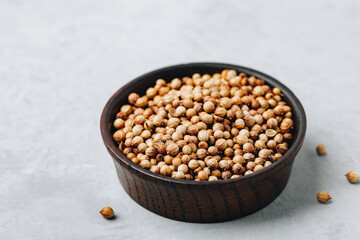 Coriander whole dry seeds in wooden bowl on gray stone background