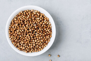 Coriander whole dry seeds in white bowl on gray stone background