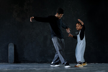 Cute little African kid boy and cool young Asian man teacher with tattoo are practice hip hop or...