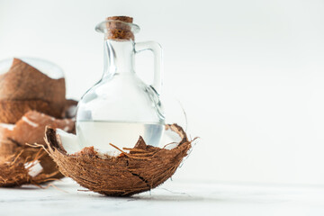 Cracked coconut with coconut oil in glass bottle on the white background