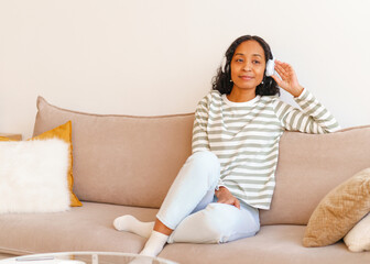 Smiling African-American female listening to music in headphones while sitting on couch