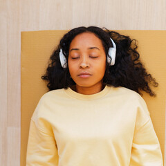 African-American woman in headphones having rest on mat with eyes closed. Relaxing after exercising