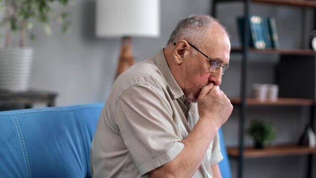 Unwell gray haired 70s elderly man coughing with seasonal flu symptoms sitting on couch at home