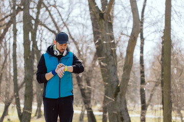 Modern technology and an active lifestyle. Smiling athlete exercises with fitness bracelet, listens to music on headphones, training for running marathon.