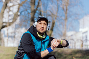 Athlete focused on running training for marathon, preparing for morning run, motivational music in headphones, athletic man turns on watch app monitoring heart rate, route.