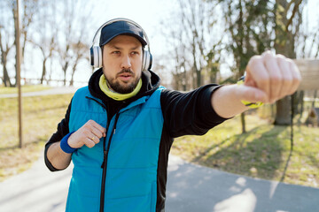 Fototapeta na wymiar Outdoor workout. Handsome young man does warm-up exercises before running while standing still, preparation for workout, boxing with hands, motivational music in headphones.