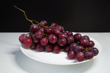 Red ripe grapes on a white plate against a contrasting background.