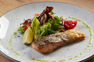 grilled fish steak on a white plate with lemon and spinach