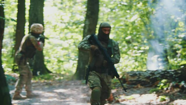 In forest two soldiers with fully equipped holds rifle wearing camouflage uniform look around running in dense forest. Stand on position