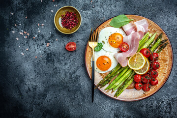 Tasty breakfast. Sunny side up eggs with green asparagus, bacon, ham and and cherry tomatoes. Healthy balanced food. Top view, above, banner