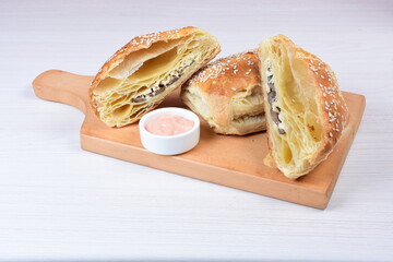 Puff pastry with mushrooms and cheese, sesame seeds and sauce on wooden background