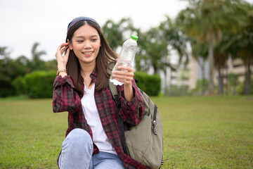 Healthy Asian woman drinking water from a bottle in the outdoor public park with green grass background.Young girl hand holding bottle drinking water.