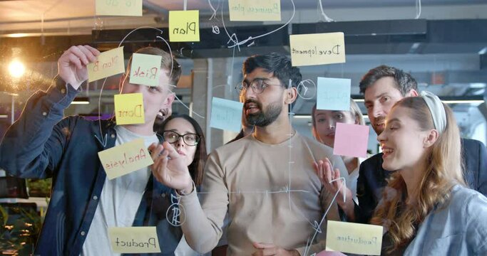 Arab man with multiethnic working team making plans for company future and sticking to-do notes. Males and females emplyees brainstorming and planning work. Head of project.