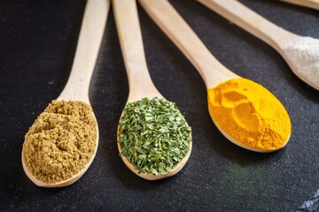 Wooden spoons filled with spices, curry, ginger, paprika, parsley, thyme, salt, on a black...