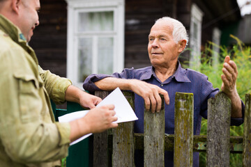 Senior man communicating with insurance company representative while standing at fence of his country house