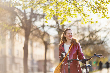 Fototapeta na wymiar happy elegant woman in red rain coat walking outside in city