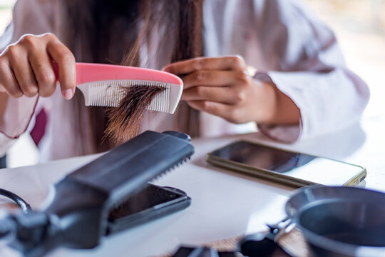 Damaged Hair, frustrated asian young woman, girl hand in holding brush splitting ends messy while combing hair, unbrushed dry long hair. Health care beauty concept.