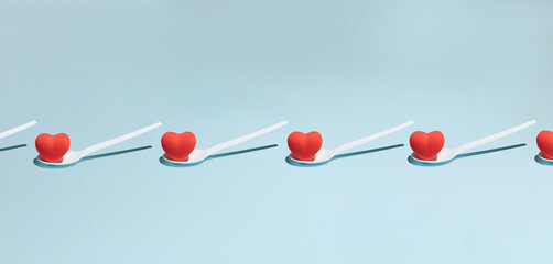 White plastic spoon with red heart on a light blue background. Minimal Valentine day concept pattern background.