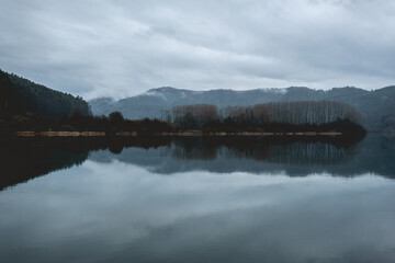 Beautiful lake in the mountains with green forest, mist,  reflections in the water and cloudy sky, Valdivia, Chile