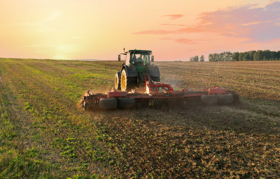 John Deere Tractor with disc cultivator Vaderstad Carrier 925 on cultivating field. Agricultural tractor on cultivation field on sunset. Soil Tillage and sowing seeds. Russia, Smolensk, Sept 07, 2021.