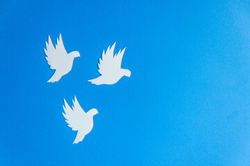 Three white paper dove birds as a symbol of peace isolated on blue background. Peace to Ukraine. World Peace Day.