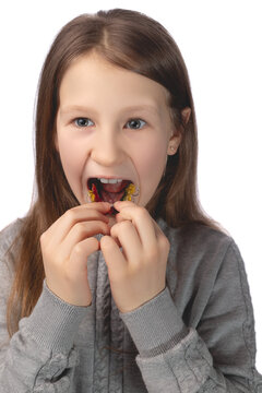 A cute little girl is putting on an orthodontic appliance. The concept of oral hygiene in childhood. Studio photo on a white background.
