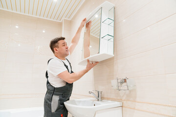 repairman hangs a bathroom mirror. accessories and furniture for bathrooms  - obrazy, fototapety, plakaty