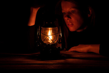 Ukrainian girl with a kerosene lamp in the dark sits at home without light