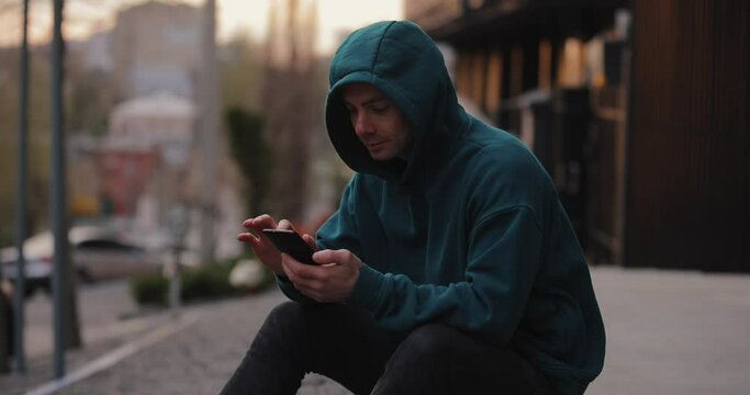 Man in hoodie using smartphone sitting in the city