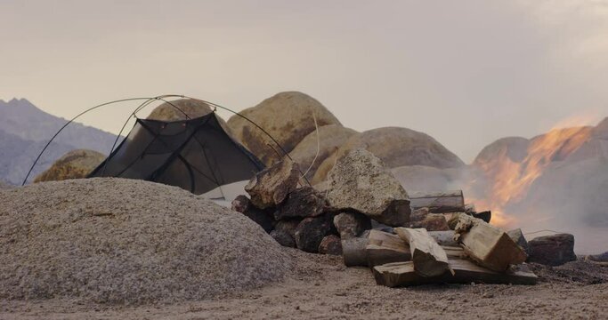Man sets up camp fire alongside tent in desert in Alabama Hills, California