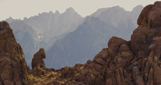Man climbs up rock formation and looks out at landscape then takes a photo in Alabama Hills, California