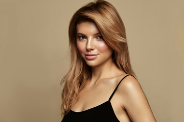 Fototapeta premium Blonde haired Woman posing against beige backgroud. Healthy Long Shiny Wavy hair. Volume shampoo. Blond Curly permed Hair and bright makeup. Beauty salon and haircare concept.