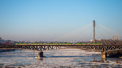 Obraz premium Warsaw, Poland - December 2021: The Cross-city Bridge, Railway bridge over the Vistula River, Train running on the bridge