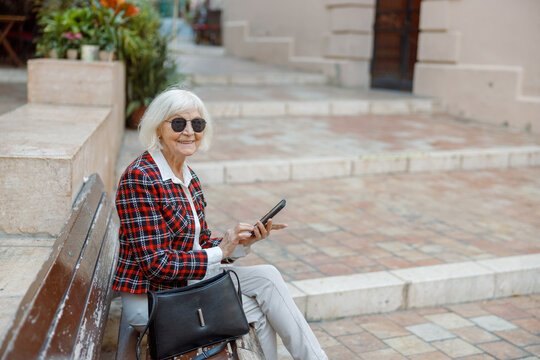 Beautiful aged woman sitting outdoors in town