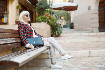 Elegant retired woman sitting outdoors in city