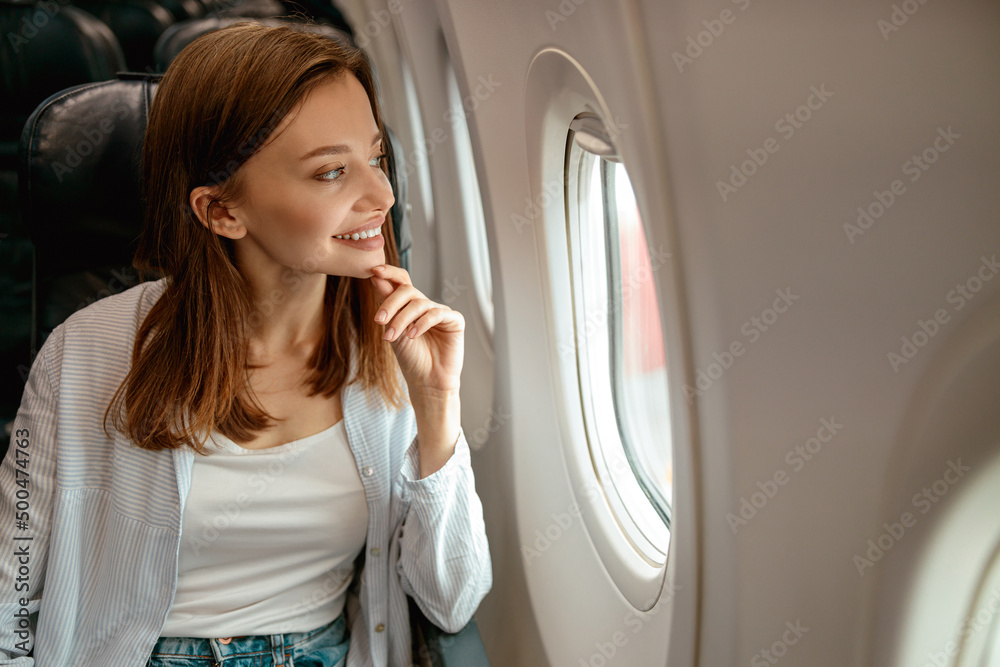 Wall mural Joyful woman looking out the window in airplane