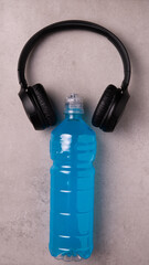 blue isotonic to replenish electrolytes and energy in a plastic bottle and wireless headphones on a concrete background