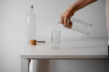 person holds a bottle and pour water in the glass