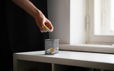 hand holds the AA electric battery and throw it in the trash bin as the symbol of recycle and reuse