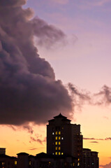 front view, far distance of a tall silhouetted building with windows glowing yellow light, at sunset on a tropical location