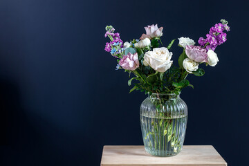 Bouquet of hackelia velutina, purple and white roses, small tea roses, matthiola incana and blue iris in glass vase isolated on black background